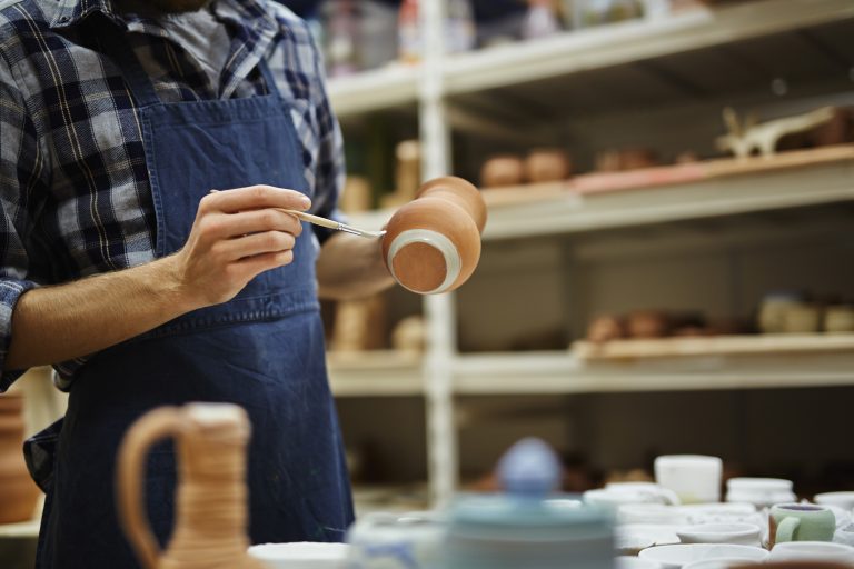 Professional potter painting jug with white paint
